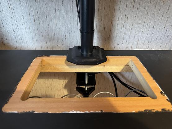 Tämä kuva näyttää pöytäkoneen tai työpisteen osan, jossa on puinen alustalaite ja musta pöytä, sekä muutamia johtoja.