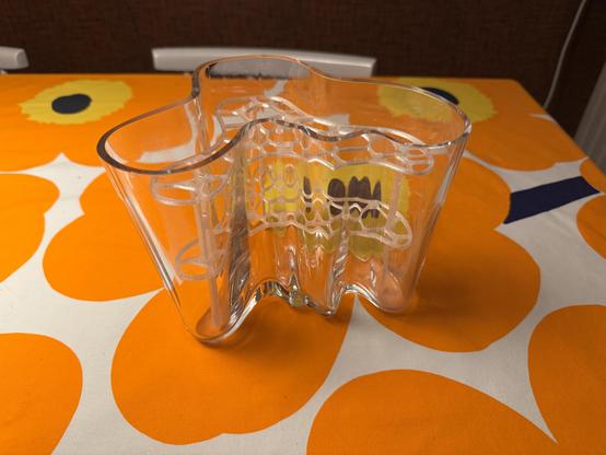 Läpinäkyvässä Aalto maljakossa 3D-tulostettu kukkatuki. Maljakko on pöydällä missä oranssilla kuosilla oleva Marimekko liina.