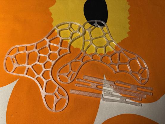 3D-tulostettu kasvituki osissa. Tuki on pöydällä missä oranssilla kuosilla oleva Marimekko liina.