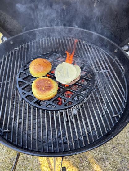 Burger pihvi ja sämpylät grillissä, liekit ja savu näkyvät.