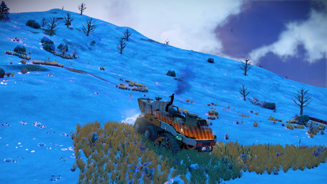 No Man’s Sky -pelin maastoajoneuvo kulkee kirkkaansinisellä, lumisella planeetalla. Kukkuloilla kasvaa harvaa kasvillisuutta ja lehdettömiä puita, ja taivaalla leijuu tummia pilviä.